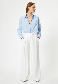 Blå skjorta med knappar och lös passform samt långa ärmar, tillsammans med vita vida byxor. Outfiten har en mjuk textur och minimal detaljering.