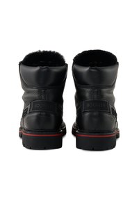 Černé kožené kotníkové boty s texturovaným povrchem, měkkou kožíškovou podšívkou a červeným akcentem na podrážce. Vedle má logové nášivky.
