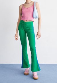 Rosa ribbat crop top med spetsdetaljer, parat med gröna utsvängda byxor med blå ränder, bärs med rosa sneakers och en ljusblå väska.