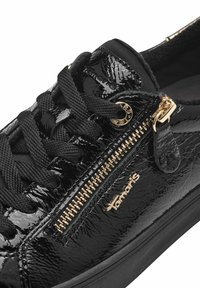 Sneaker in pelle verniciata nera con accenti dorati, caratterizzato da una cerniera laterale e una superficie testurizzata; lacci neri e dettaglio del logo del marchio.
