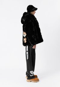 Chaqueta de piel sintética negra con un diseño de oso bordado en la espalda. Combinada con jeans negros y zapatos marrones con suela gruesa.