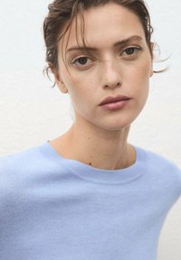 Light blue knitted sweater with a round neckline, featuring a smooth texture and subtle stitching detail at the hem and sleeves.