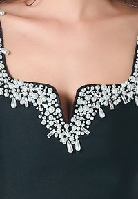 Robe noire avec un décolleté en V orné de grappes de perles blanches et d'accents transparents, créant un effet décoratif texturé.
