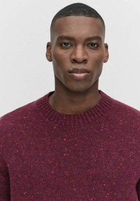 Bordeaux gebreide trui met een geribde hals, voorzien van spikkels in rood en blauw, die een gestructureerd oppervlak en een klassieke pasvorm toont.