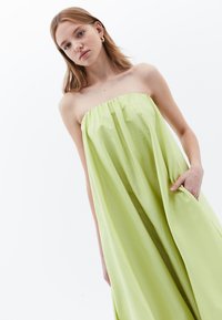 Trägerloses, limegrünes Kleid aus leichtem Stoff. Verfügt über einen gerafften Ausschnitt und Seitentaschen. Glatte Textur und fließendes Design.