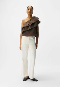Brun en skuldertop med lagdelte volanger; parret med hvide vide bukser og sorte flade sko. Sort hår trukket tilbage, minimale accessories.