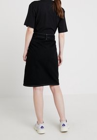 Falda de mezclilla negra con corte recto, costuras visibles y cinturilla. Combinada con zapatillas blancas con detalles en púrpura.