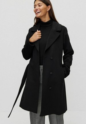 Black trench coat featuring a single-breasted design, large lapels, and button closures. Smooth texture with a tied belt at the waist.
