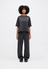T-shirt oversize grigio scuro in cotone con un piccolo logo rosso, abbinato a pantaloni larghi coordinati e sneakers nere.