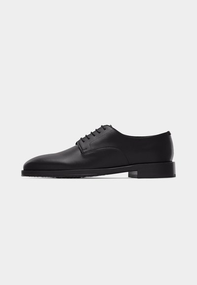 Chaussure Oxford en cuir noir pour hommes, avec laçage fermé et petit talon empilé, vue de profil sur fond blanc.