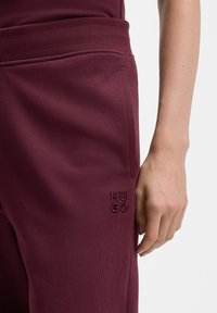 Bordowe spodnie dresowe wykonane z miękkiego materiału, z elastycznym paskiem w talii i bocznymi kieszeniami. Logo „HUGO” wyhaftowane na lewej udzie.