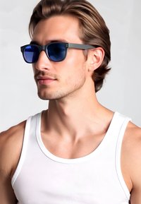 Occhiali da sole con lenti blu e montatura nera opaca con sottili accenti verdi, indossati con una canotta bianca su uno sfondo chiaro.