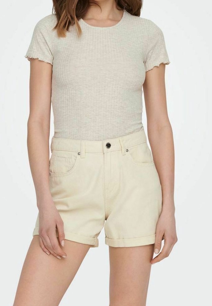 Femme portant un haut beige côtelé ajusté à manches courtes et un short crème taille haute avec ourlet roulotté, debout devant un fond uni.