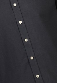 Camicia nera con bottoni in cotone. Presenta un'apertura con sei bottoni beige chiaro e una texture morbida e liscia.