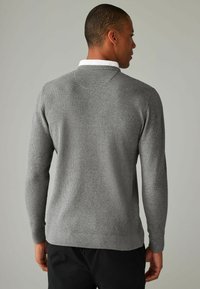 Pull en maille grise avec un motif texturé, col rond et manches longues, présentant un col blanc contrastant en dessous.