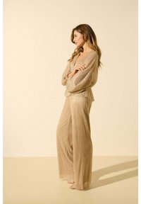 Ensemble deux pièces beige scintillant comprenant un haut ample et drapé ainsi que des pantalons à jambes larges avec une finition métallique texturée.