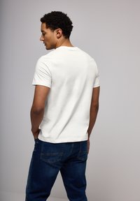 White cotton t-shirt with a crew neck, short sleeves, and a relaxed fit, paired with dark blue denim jeans. Simple design, no visible logos.