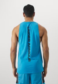 Lys blå tanktopp i stoff, med en iøynefallende svart "UNDER ARMOUR" logo vertikalt langs ryggen. Ermeløs design, løs passform.