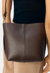 Bruine leren emmer tas met een gladde textuur, heeft een naad in het midden en een korte strap bevestigd met metalen hardware.
