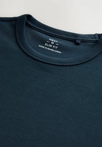 Donker marineblauw slim fit t-shirt, geribbelde textuur, ronde halslijn, label zichtbaar met merk- en productiedetails.