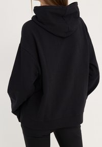 Sudadera con capucha negra con cordón, ajuste holgado y puños acanalados. Textura de tela suave, diseño sencillo sin estampados ni adornos.