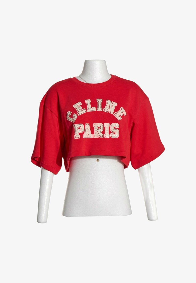 T-shirt rouge court avec manches larges présenté sur un mannequin de torse blanc, avec un texte blanc "CELINE PARIS" à l'avant.