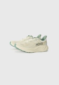 Sportliche Schuhe mit einem cremefarbenen Obermaterial, grünen Akzenten, strukturiertem Mesh-Material und einer gepolsterten Sohle mit einem gemusterten Profil.