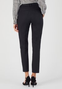 Pantaloni neri su misura con una vestibilità slim, caratterizzati da una superficie liscia, passanti per cintura e tasche posteriori, abbinati a scarpe nere con tacco alto.