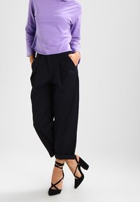 Maglietta viola a maniche lunghe abbinata a pantaloni neri a vita alta con pieghe e scarpe con tacco a strappo, caratterizzati da una texture liscia e un taglio rilassato.