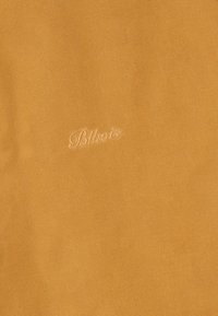 Sininen keltainen kangas, jossa on hienovaraisesti brodattu "Blkovois" -teksti yhdistelevällä langalla keskellä.