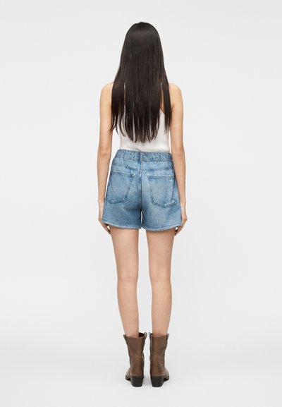 Shorts en jean bleu clair avec une coupe décontractée, une taille élastique et deux poches arrière. Portés avec des bottines marron.