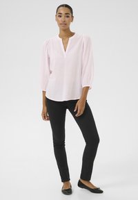 Blouse rose clair avec un col rond et des manches mi-longues, arborant un motif texturé subtil. Associée à un pantalon noir slim et des ballerines.