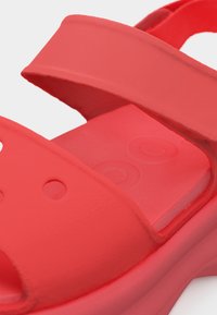 Κόκκινο σανδάλι με ανοιχτά δάχτυλα, ρυθμιζόμενα λουριά και αναπαυτική σόλα με κυκλικά αποτυπώματα.