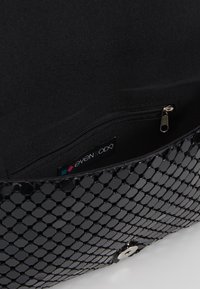 Musta verkkomallinen käsilaukku, jolla on rakenteellinen muoto. Sisällä on vetoketjullinen tasku ja sileä vuori. Hopeiset yksityiskohdat suljinnassa.