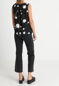 Top senza maniche nera con motivo floreale bianco, abbinato a jeans cropped scuri e sandali con plateau neri. Tessuto morbido, vestibilità rilassata.