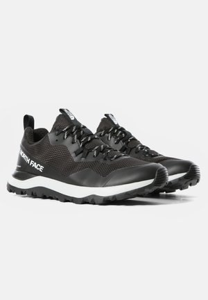 Par de zapatillas de trail running negras de North Face con medias suelas blancas, suelas exteriores resistentes, cordones con estampado y empeines de tela de malla.