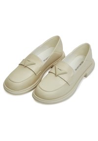 Mocassini in pelle beige con una fascia diagonale decorativa e logo dorato, dotati di punta rotonda e suola in gomma bassa e testurizzata.