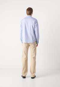 Lichtblauw overhemdd, beige rechte broek en zwarte schoenen. Het overhemd heeft een standaard kraag en knoopmanchetten, met minimale details.