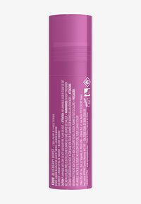 Flytande rouge i en cylindrisk behållare, matt lila lock, genomskinlig kropp som avslöjar en rosa produkt, med fler språk-text på sidan.