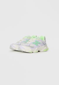 Des baskets violettes et vertes en matériau en maille et synthétique, présentant une semelle épaisse, des lacets proéminents et un accent vert au niveau du talon.
