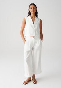 Gilet bianco tagliato con colletto a rever e un bottone, abbinato a pantaloni bianchi larghi con cordoncino e risvolti.