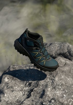Donker teal wandelshoe met zwarte accenten, bovenwerk van textuurstof en robu sole. Heeft gele stiksels en een vetersluiting.
