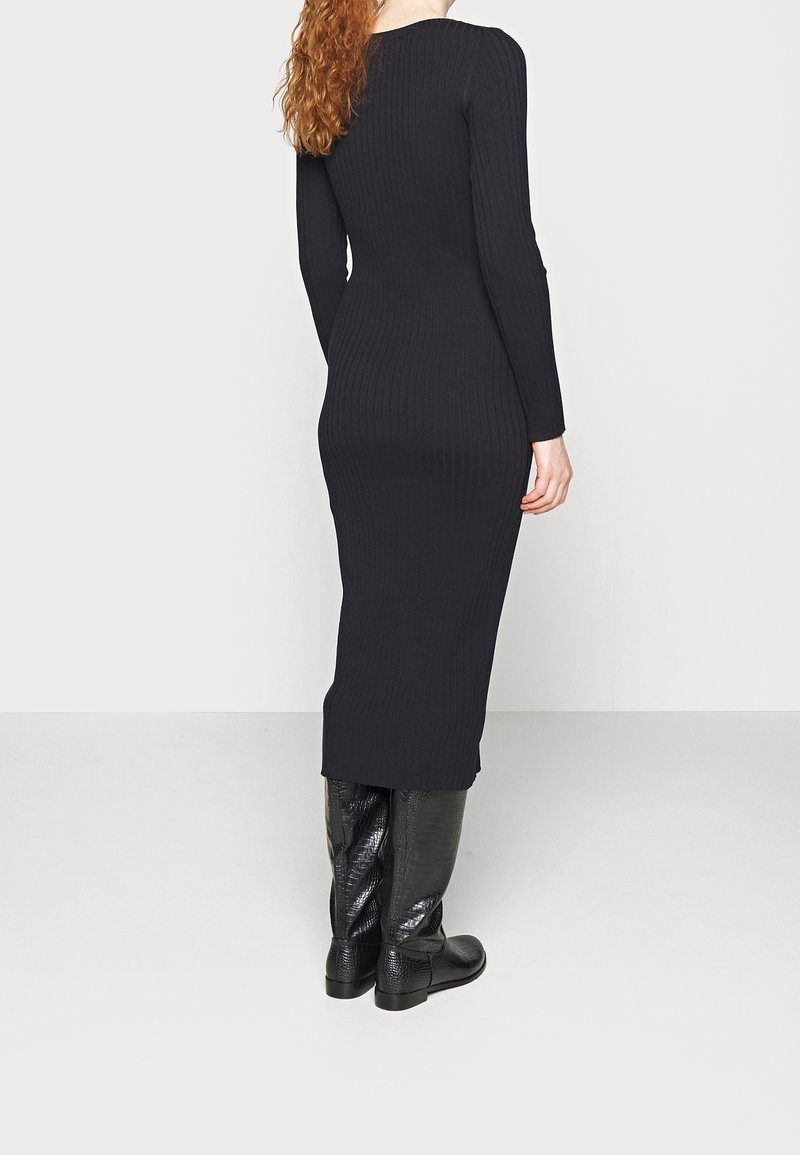 Vestido negro de manga larga con textura acanalada y silueta ajustada. El vestido tiene un escote redondo y llega a la mitad de la pantorrilla, combinado con botas de textura hasta la rodilla.