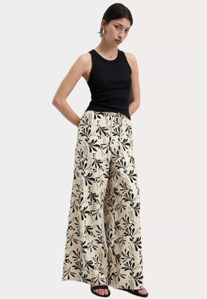 Svart ärmlös topp kombinerad med vida krämfärgade byxor med svart blommönster. Ärmlös design och elastisk midja.