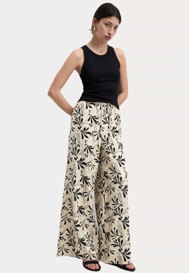 Zwarte mouwloze top gecombineerd met crème wijd uitlopende broek met een zwart bloemenpatroon. Mouwloos ontwerp en elastische tailleband.