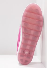 Semelle de basket rose avec une bande de roulement en caoutchouc translucide, une semelle intermédiaire blanche et une unité de coussinage circulaire près du talon, positionnée sur des surfaces blanches.