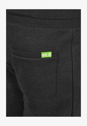 Czarne dresy z prążkowanym pasem, tylną kieszenią i jasną zieloną metką "!SOLID" na kieszeni. Miękka, teksturowana tkanina.