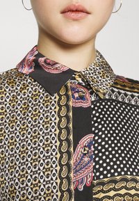Koszulka z kołnierzykiem w wielu kolorach, z mieszanką wzorów paisley, geometrycznych i w kropki na czarnym tle z złotymi akcentami.