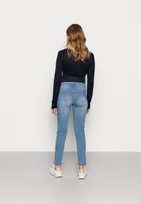 Jeans skinny de color azul claro con una textura suave, bolsillos traseros y ligero estiramiento. Combinados con una camiseta negra ajustada de manga larga y zapatillas blancas.