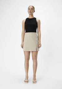 Svart ribbad linne och beige minikjol med en framficka. Modellen bär vita öppna sandaler. Minimalistisk design, mjuka texturer.